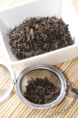 Fototapeta premium black tea leaves in white bowl with strainer on bamboo mat