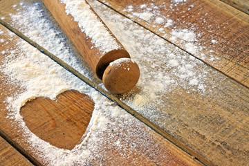 flour, rolling pin and heart with wood background