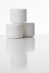Drei weiße Cremedosen übereinander gestapelt mit Spiegelung
