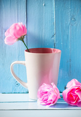 Mug with pink roses on blue wood background, still life