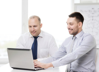 Obraz premium two smiling businessmen with laptop in office