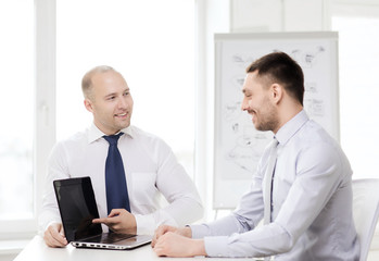 two smiling businessmen with laptop in office