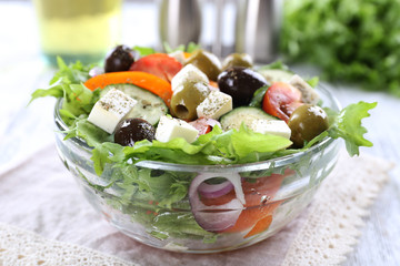 Greek salad in glass dish on napkin and color wooden background