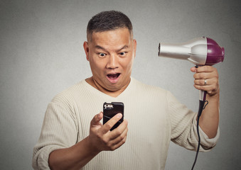 shocked surprised man looking on smartphone holding hairdryer