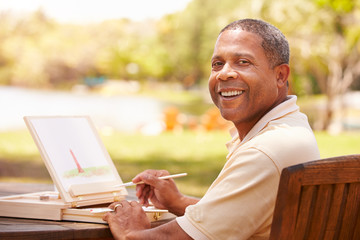 Senior Man Sitting At Outdoor Table Painting Landscape