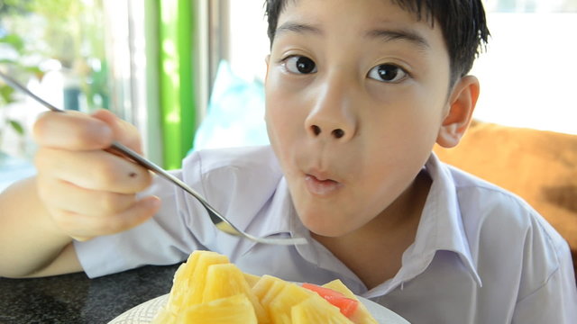 Little asian cute boy eating piece of ripe pineapple .