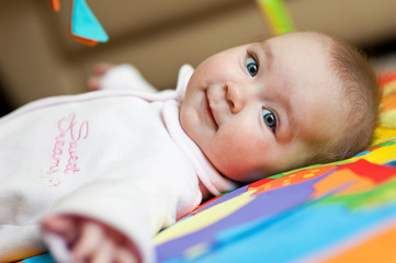 newborn infant baby girl lying on back on colorful carpet