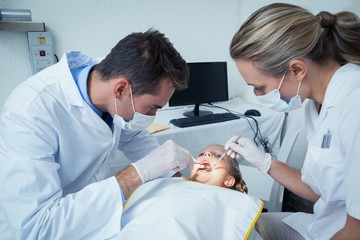 Dentist examining girls teeth with assistant