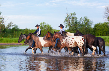 Two cowboys on horses ford the river