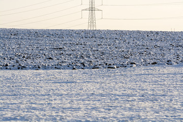 Electricity power pylon at a plowed field covered with snow