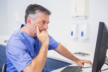 Serious dentist sitting and using computer - obrazy, fototapety, plakaty