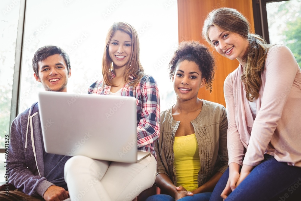 Poster smiling students sitting on couch using laptop