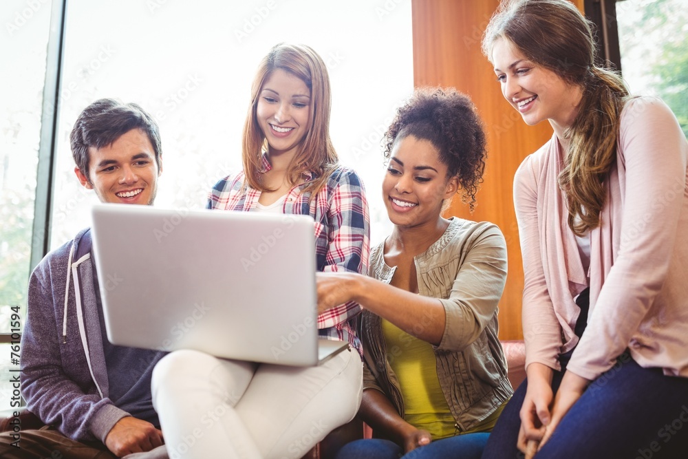 Poster smiling students sitting on couch using laptop