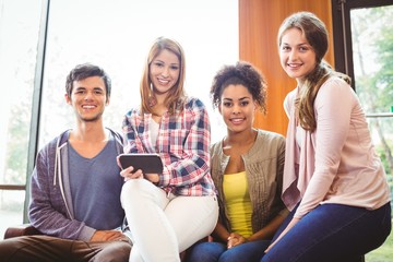 Happy students sitting on a sofa using mobile phone