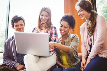 Smiling students sitting on couch using laptop