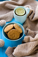 A cup of tea with lemon, biscuits, beige knitted blanket