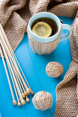 Fototapeta na wymiar A cup of tea with lemon, beige knitted blanket and spokes