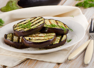 Grilled eggplant slices on a plate with fresh herbs.