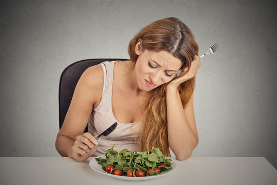 sad displeased young woman eating salad grey wall background 