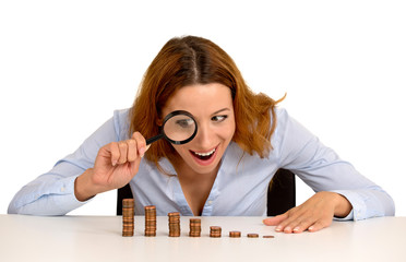 woman looking at growing stack of coins through magnifying glass