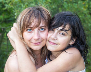 Young woman hugging her teenager daughter, summer outdoors.