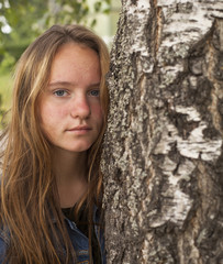 Young cute teen girl with long hair portrait near the tree.