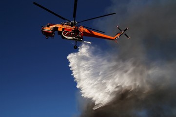 Fototapeta na wymiar Firefigthers are fighting with bushfire. Helicopter drops water from the sea