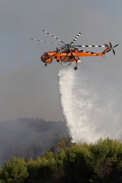Firefigthers are fighting with bushfire. Helicopter drops water from the sea
