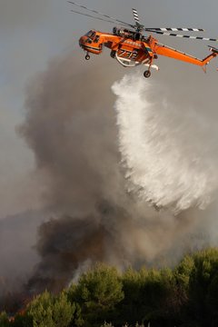 Firefigthers are fighting with bushfire. Helicopter drops water from the sea