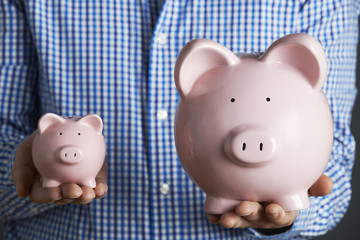 Man Holding Large And Small Piggy Bank
