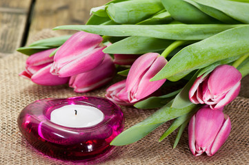 Purple tulips on old wooden table next to a candle burns