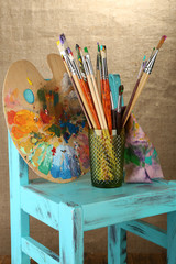 Paint brushes with paints and palette on beige background