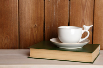 Cup of hot drink on book on tabletop and wooden background