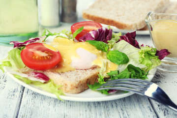 Toast with egg Benedict and tomato on plate on wooden table