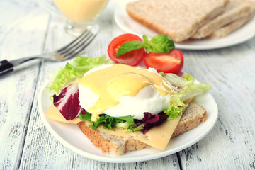Toast with egg Benedict and tomato on plate on wooden table