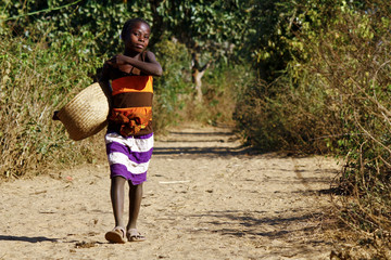 Poor african girl walking the african path with basket in hand