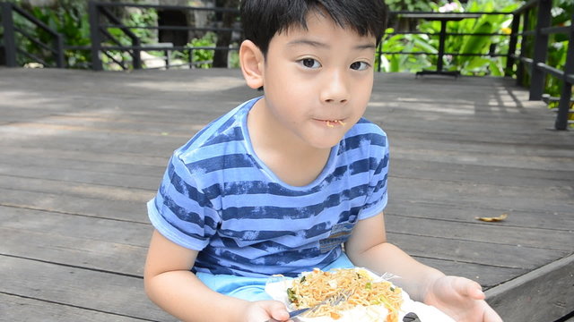 young asian cute boy eating fried chiness noodles.
