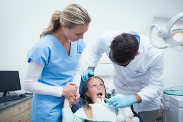 Obraz premium Dentist with assistant examining girls teeth