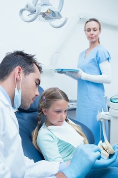 Male dentist teaching girl how to brush teeth