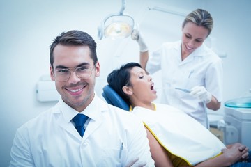 Fototapeta premium Smiling male dentist with assistant examining womans teeth