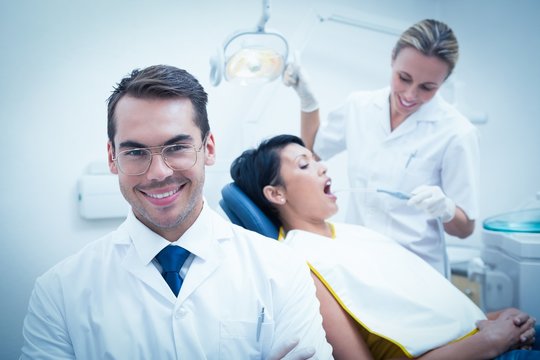 Smiling male dentist with assistant examining womans teeth