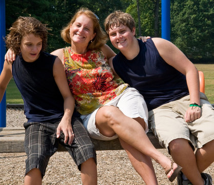 mother and two sons being playful on park bench