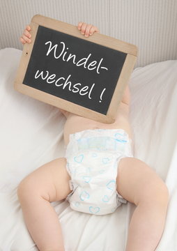 Baby hält Tafel mit Aufschrift Windelwechsel