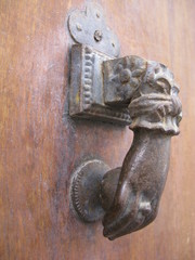Heurtoir en métal en forme de mains sur une porte ancienne en bois