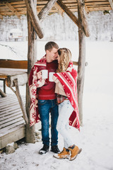 Happy couple wrapped in plaid drink hot tea in a snowy forest 