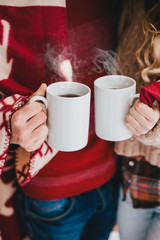 Happy couple wrapped in plaid drink hot tea in a snowy forest 