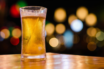 Glass of beer with bokeh bar scene in the background.