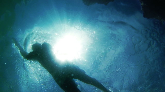 Swimming men silhouette with sun rays from bottom camera