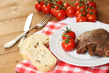 Roasted meat and vegetables on plate, on wooden table
