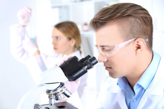 Young Female And Male Scientists  With Microscope In Laboratory